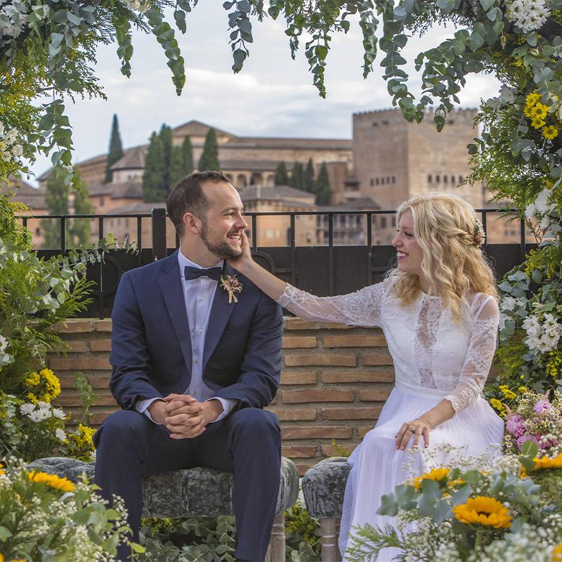 bodas-elcamborio-granada-galeria-7 Novios durante ceremonia civil exterior con la alhambra de granada de fondo y decoración floral