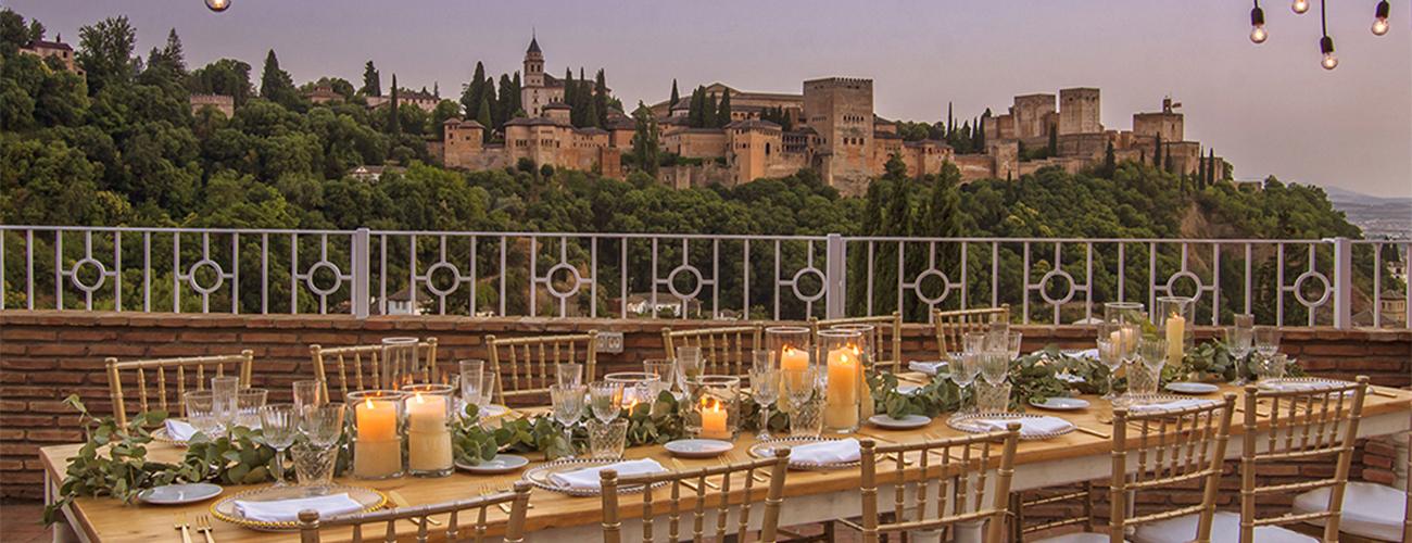 Mesa larga preparada para boda en El Camborio, elegantemente decorada, con la Alhambra de Granada visible al fondo.