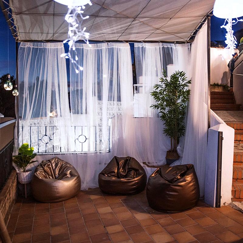 elcamborio-eventos-sociales-granada-22 Zona relax en la terraza de El Camborio durante un evento corporativo de noche, con tres pufs y ambiente iluminado.
