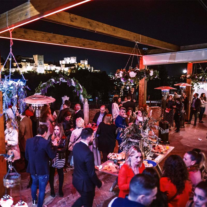 elcamborio-eventos-sociales-granada-23 Invitados disfrutando de un evento corporativo tipo cóctel en la terraza de El Camborio durante la noche, con iluminación ambiental elegante