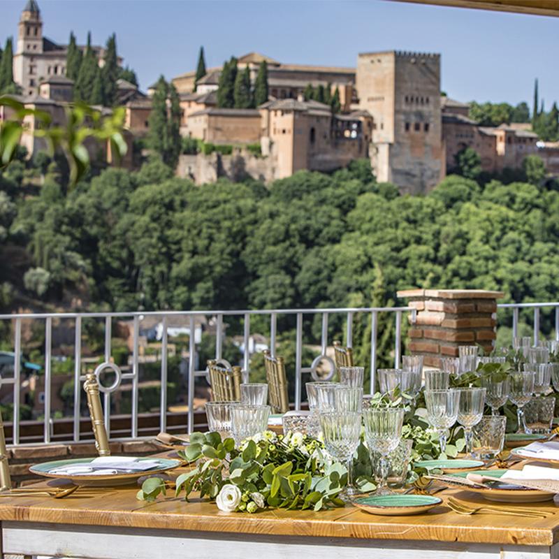 elcamborio-eventos-sociales-granada-6 Mesa al aire libre preparada para una boda en El Camborio, con elegantes detalles y vistas panorámicas de la Alhambra de Granada.