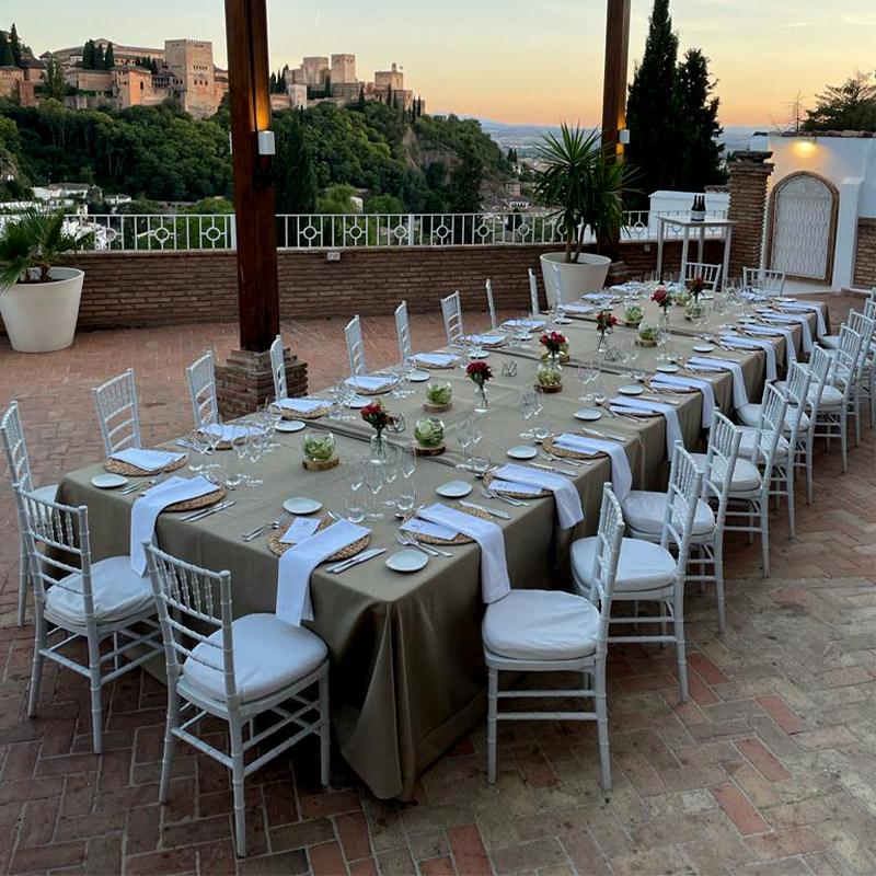 eventos-corporativos-elcamborio-granada-13 Mesa única para un evento social en la terraza de El Camborio, con la Alhambra de Granada visible al fondo.