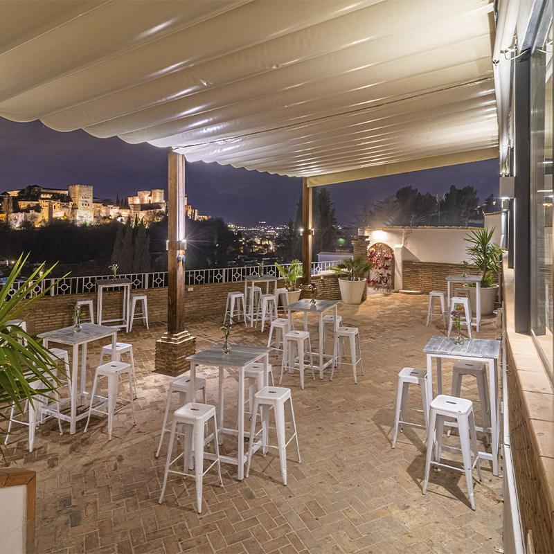 eventos-corporativos-elcamborio-granada-14 Zona de cóctel en la terraza de El Camborio preparada para un evento social, con la Alhambra de Granada visible al fondo.