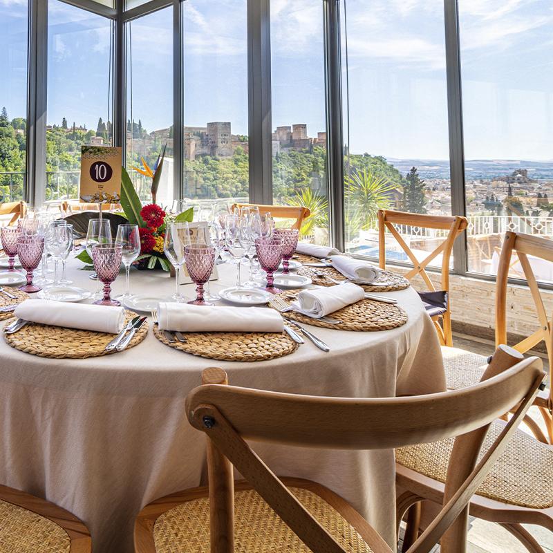 Montaje de mesa de boda en salón interior de El Camborio con vistas a la Alhambra de día a través de la cristalera"