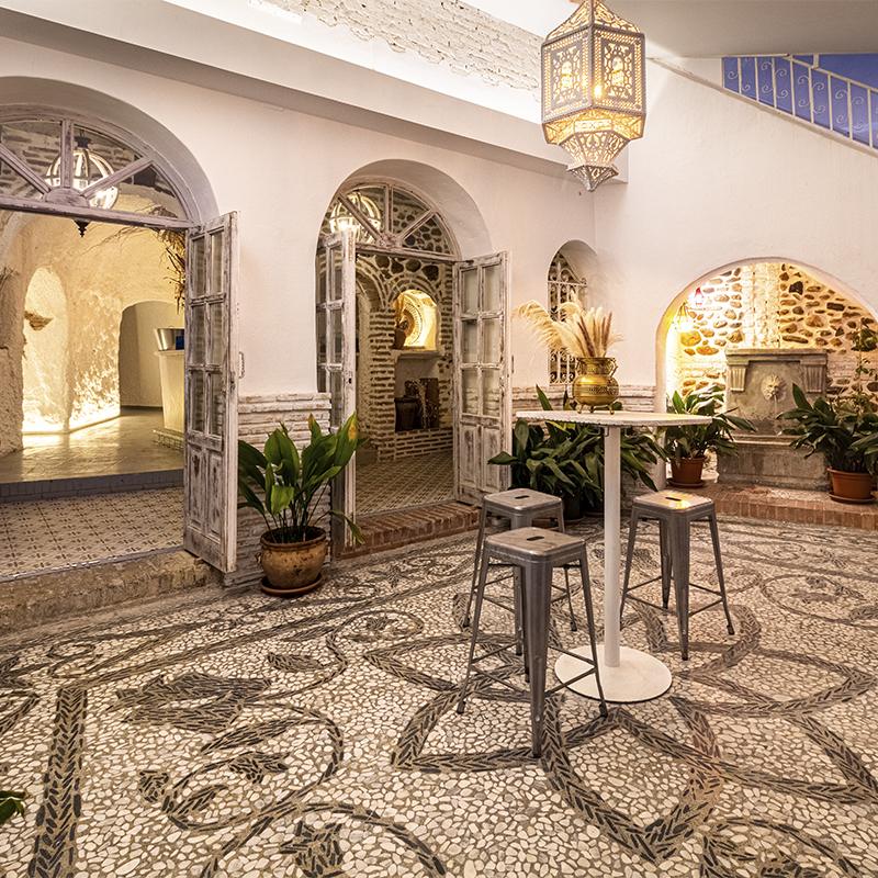 Patio interior de la parte baja del edificio decorado de estilo clásico granadino con piedras y madera en tonos blancos y grises con lampara estilo mozárabe